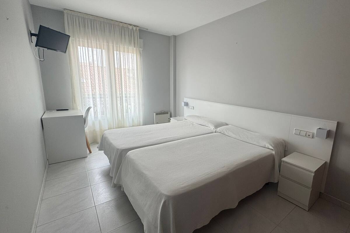 Una habitación de hotel limpia y moderna, con dos camas, un escritorio y un televisor montado en la pared.