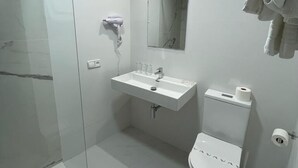 Un baño moderno con cabina de ducha de vidrio, un lavamanos blanco, un espejo y un inodoro.