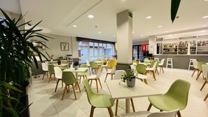 Un comedor moderno con sillas verdes y blancas, mesas blancas y una zona de bar con estantes llenos de botellas.