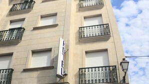 Fachada de un hotel con un letrero que dice "HOTEL", un balcón con barandilla de hierro forjado y una entrada a nivel de calle con una puerta que indica "HOTEL".