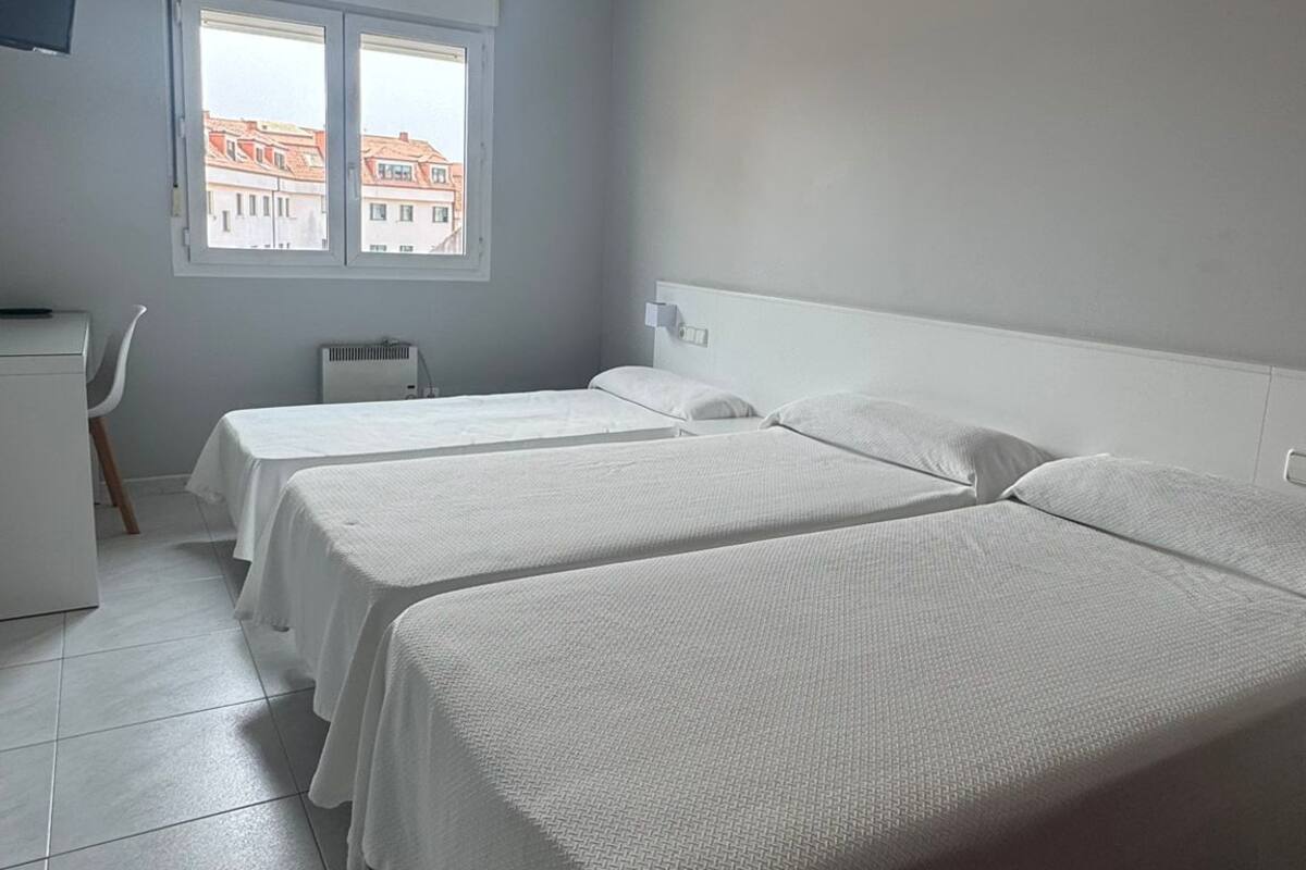 Una habitación con dos camas, un escritorio y un ventanal con vistas a edificios.