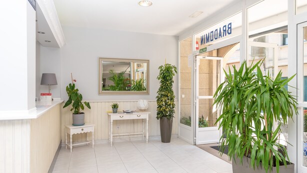 Un área de recepción con una consola blanca, un espejo, una planta en maceta, un escritorio y una puerta con la leyenda 'BRADFORD'.