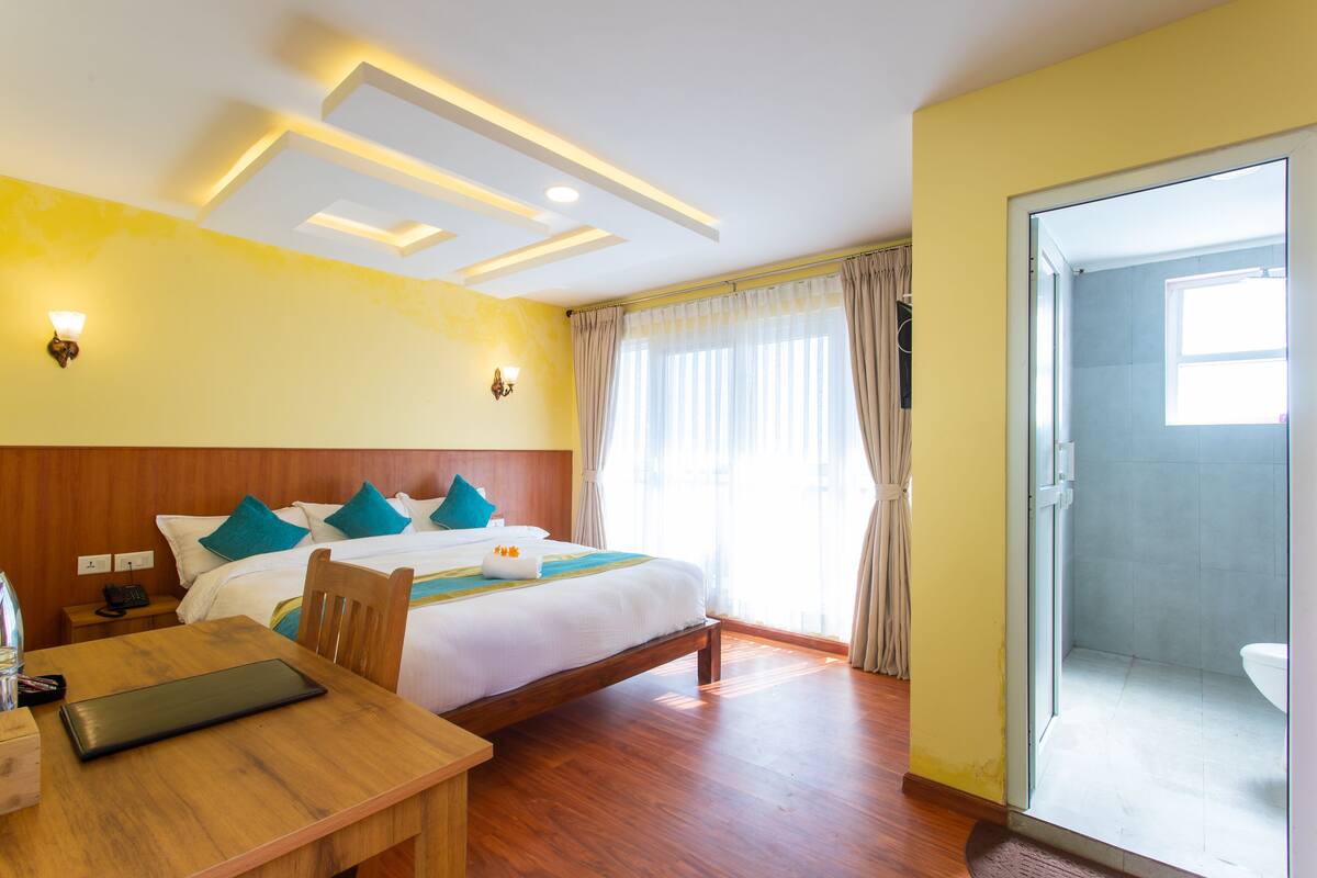 A hotel room with a bed, bedside table, and a bathroom with a shower and toilet.