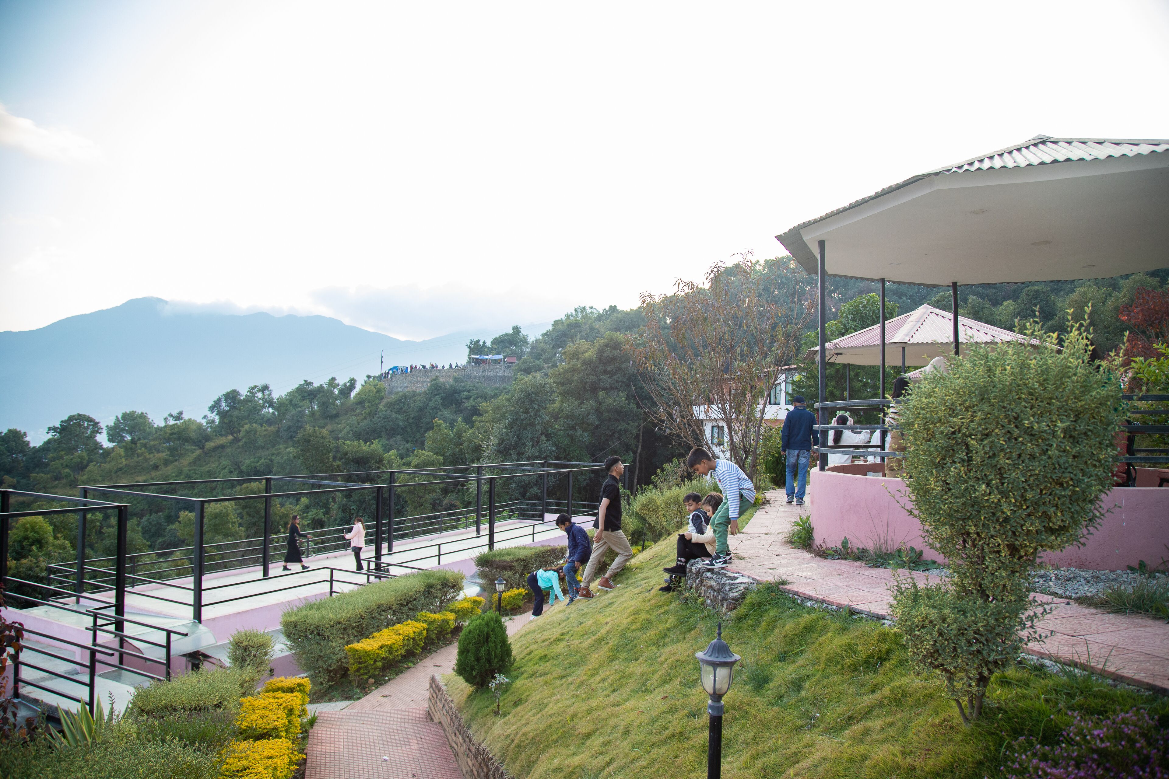 A hillside walkway with a metal railing, a lamp post, and a covered area with a roof.