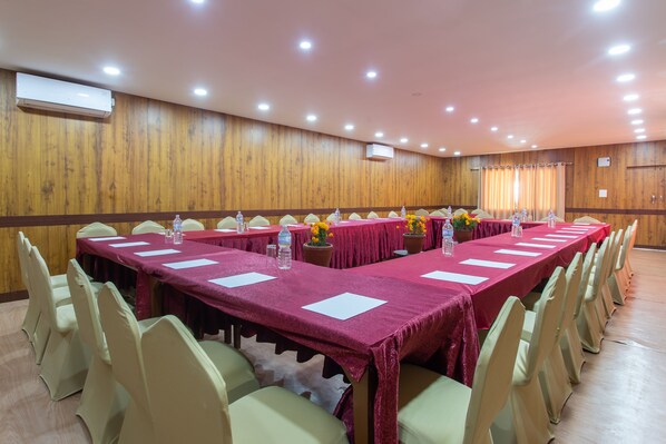 Un salón de conferencias con mesas largas, sillas y centros de mesa florales.