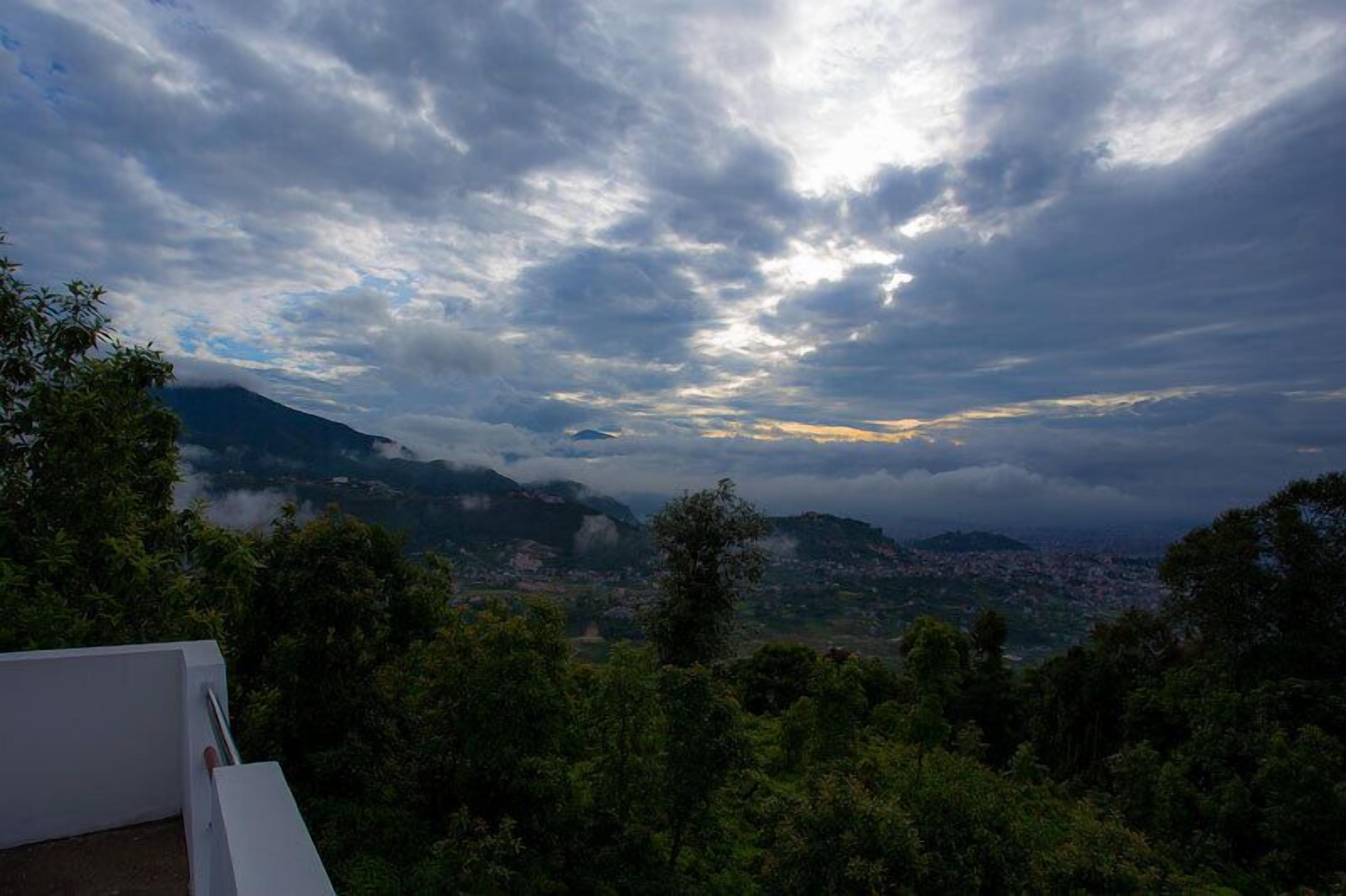 A mountainous landscape with a town below, under a cloudy sky.