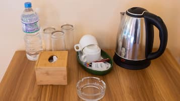 A wooden table with a water bottle, four glasses, a white mug, a sugar packet, a glass ashtray, and a kettle.
