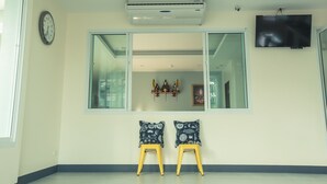 Ein Zimmer mit großem Fenster, Klimaanlage, Fernseher und zwei Stühle mit gemusterten Kissen.