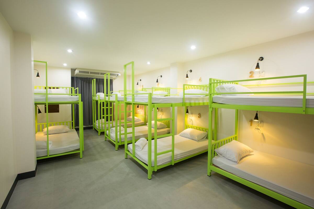 A dormitory room with bunk beds, a window with curtains, and a wall-mounted air conditioning unit.