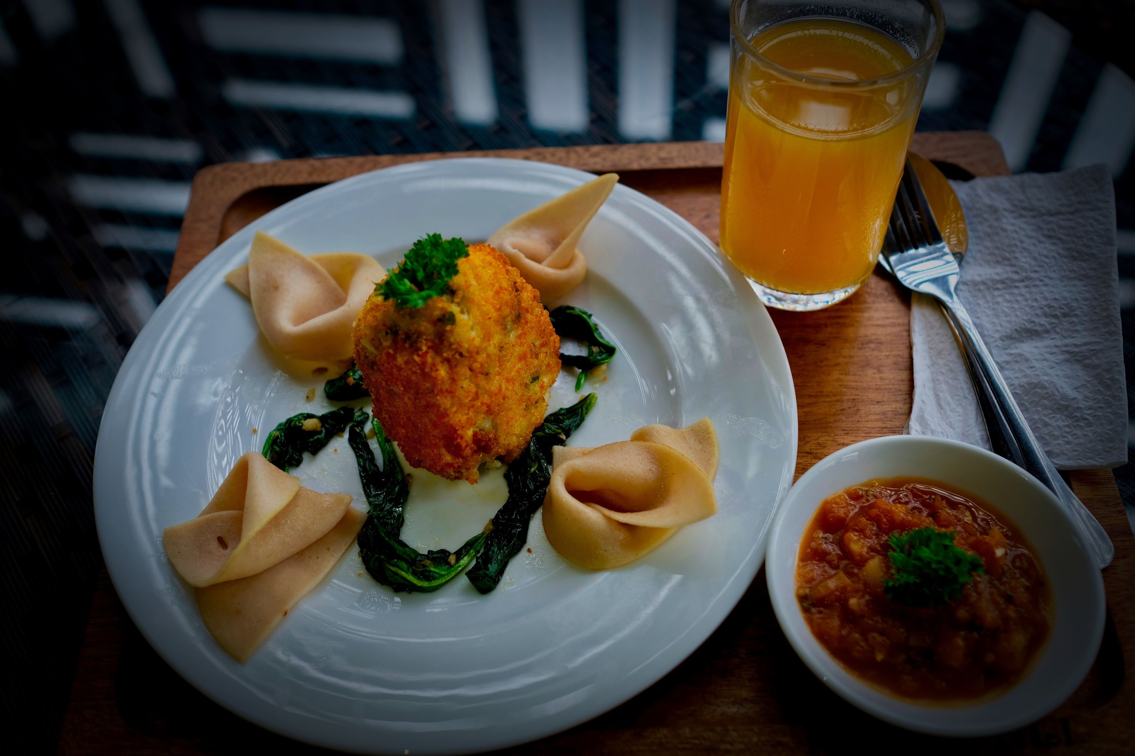 Un plato de comida que incluye dumplings, un alimento empanizado y un tazón de salsa, acompañado de un vaso de jugo de naranja.