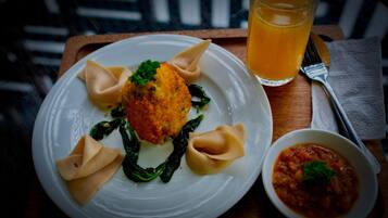 Un plato de comida que incluye dumplings, un alimento empanizado y un tazón de salsa, acompañado de un vaso de jugo de naranja.