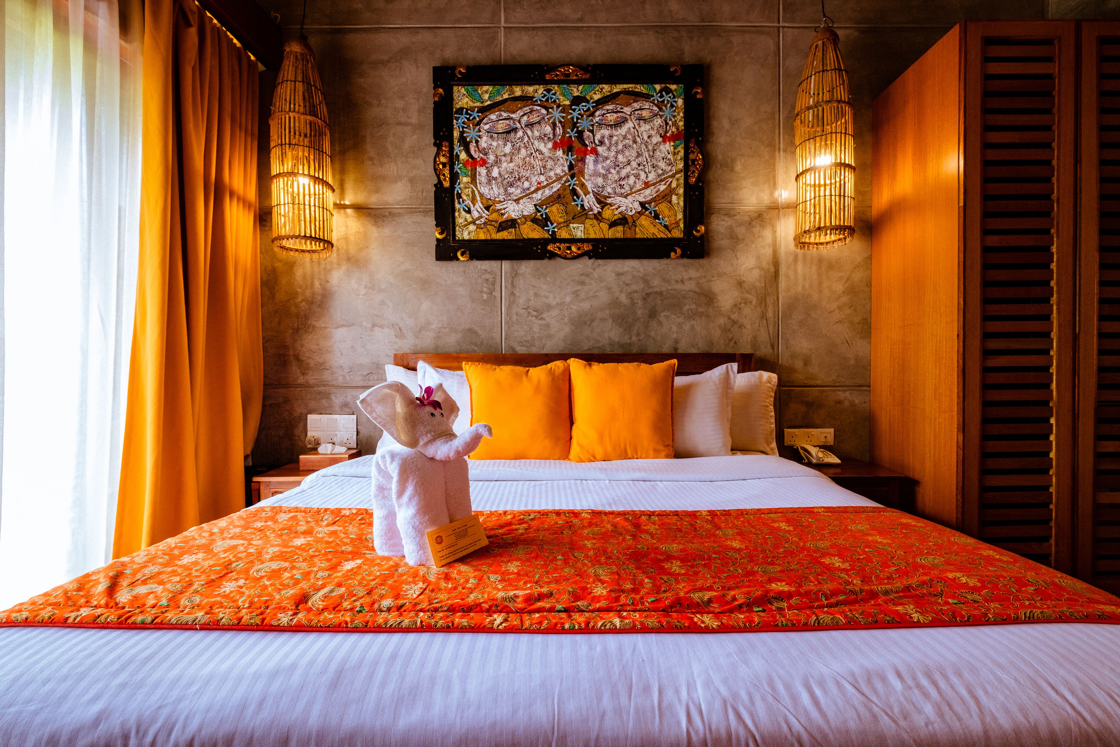 Ein Hotelzimmer mit einem großen Bett, orangefarbener Bettwäsche, einem dekorativen Gemälde und zwei Wandleuchten.