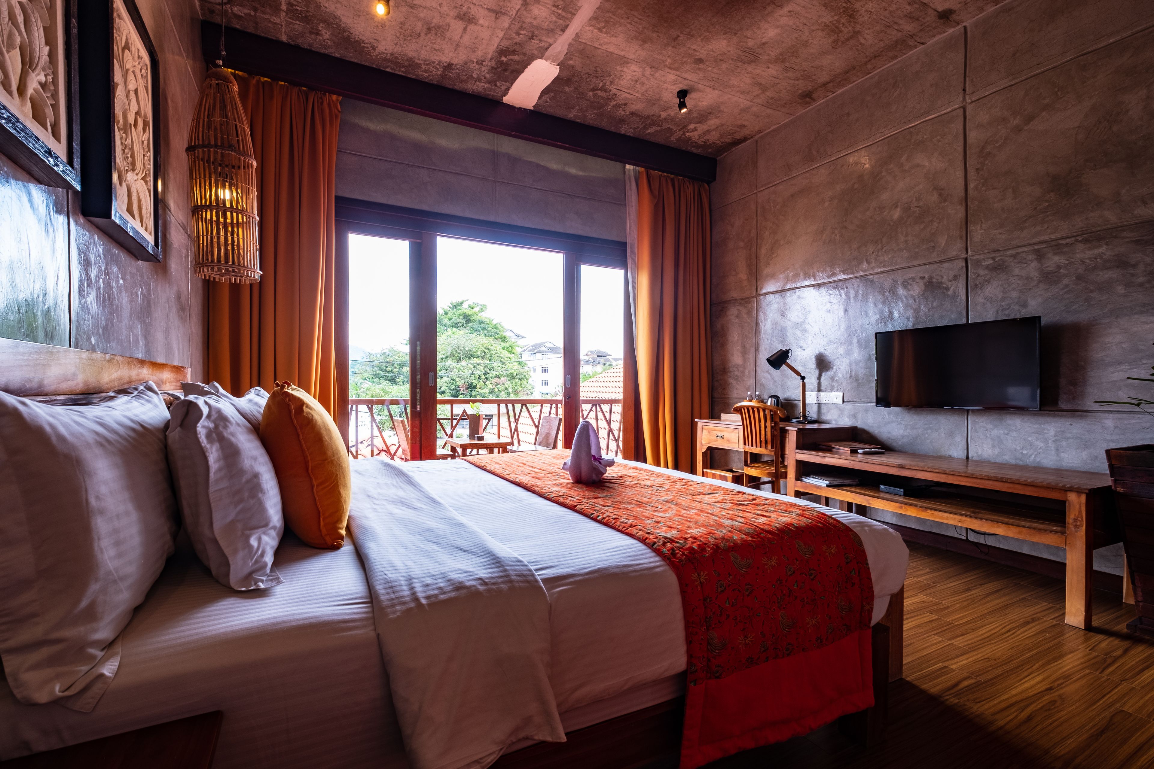 A hotel room with a large bed, wooden furniture, a television, and a balcony with a view.
