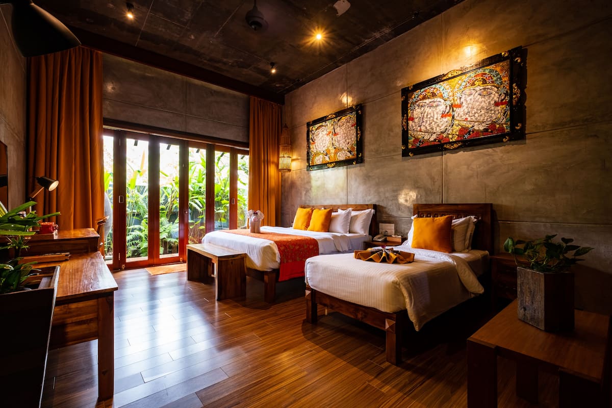 A hotel room with two beds, wooden furniture, a large window with curtains, and artwork on the walls.