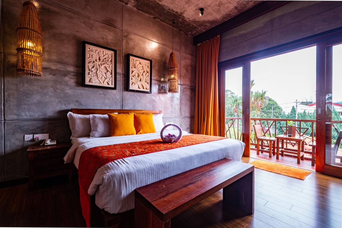 A bedroom with a large bed, wooden bench, and a balcony with outdoor furniture.