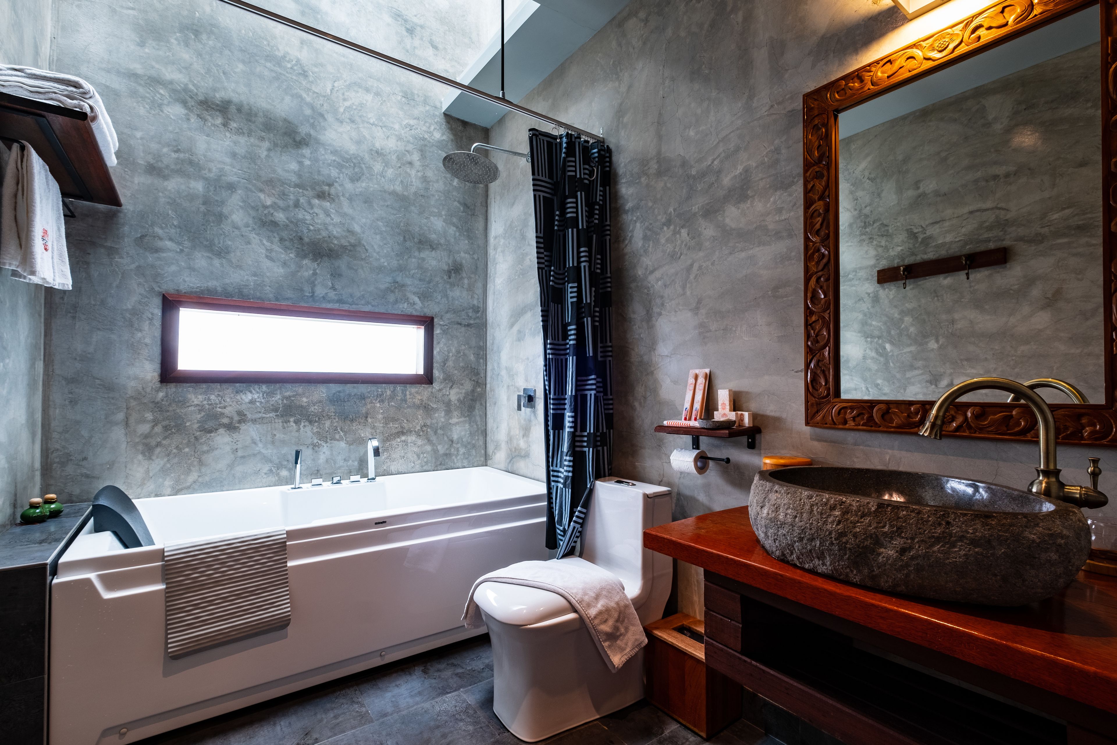 A modern bathroom with a large bathtub, a stone sink, a toilet, and a shower.