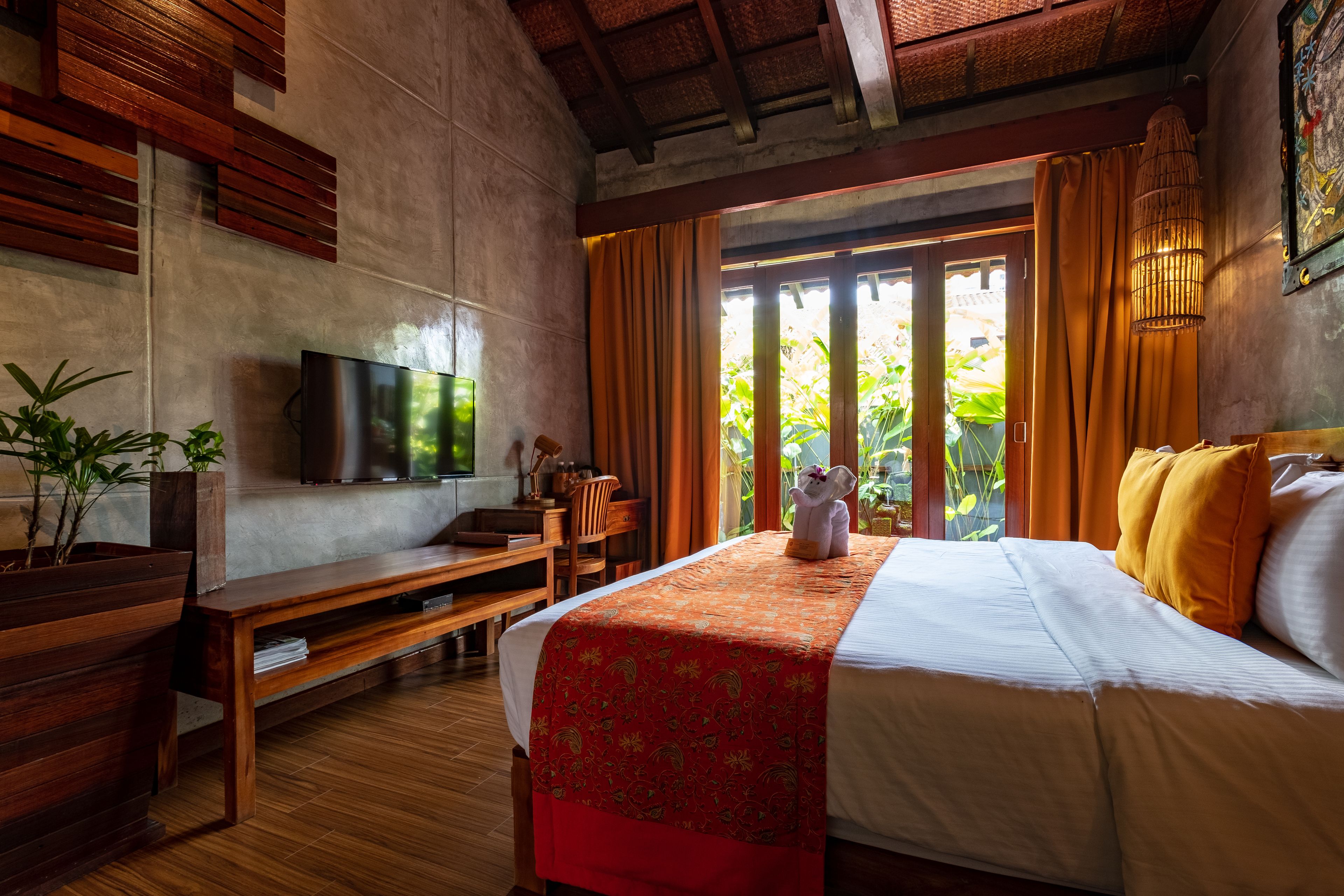 A hotel room with a large bed, wooden furniture, a TV, and a view of greenery outside.