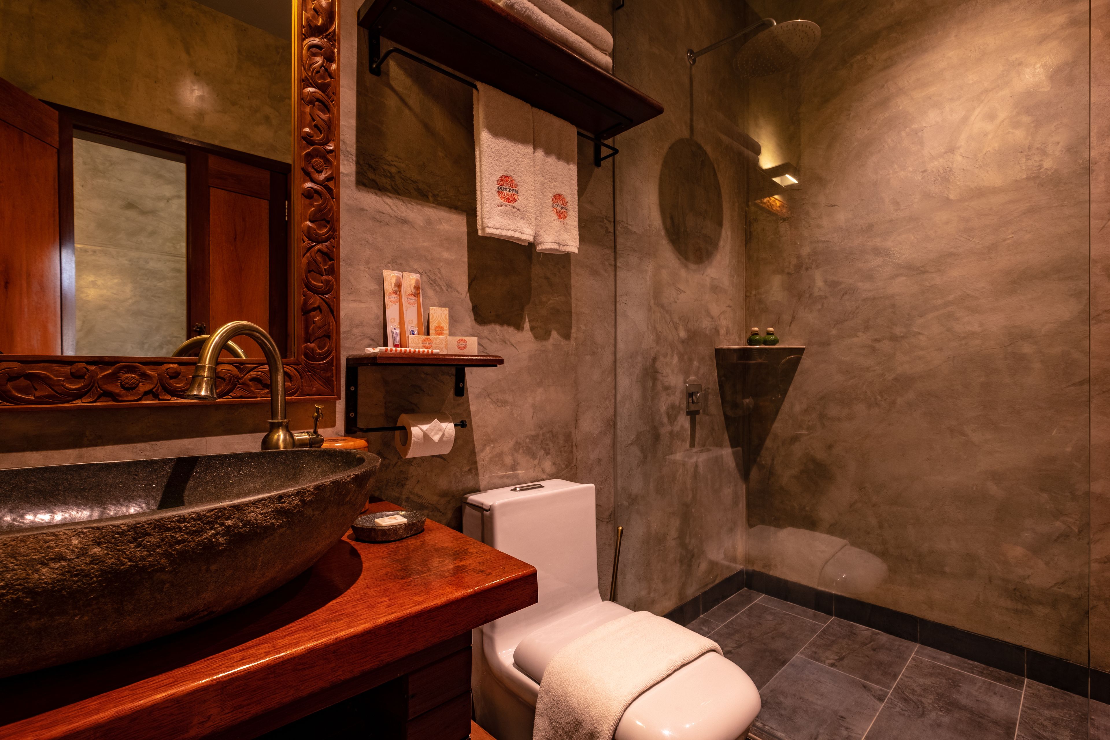 A bathroom with a large stone sink, a wooden vanity, a white toilet, and a shower area.
