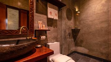 A bathroom with a large stone sink, a wooden vanity, a white toilet, and a shower area.