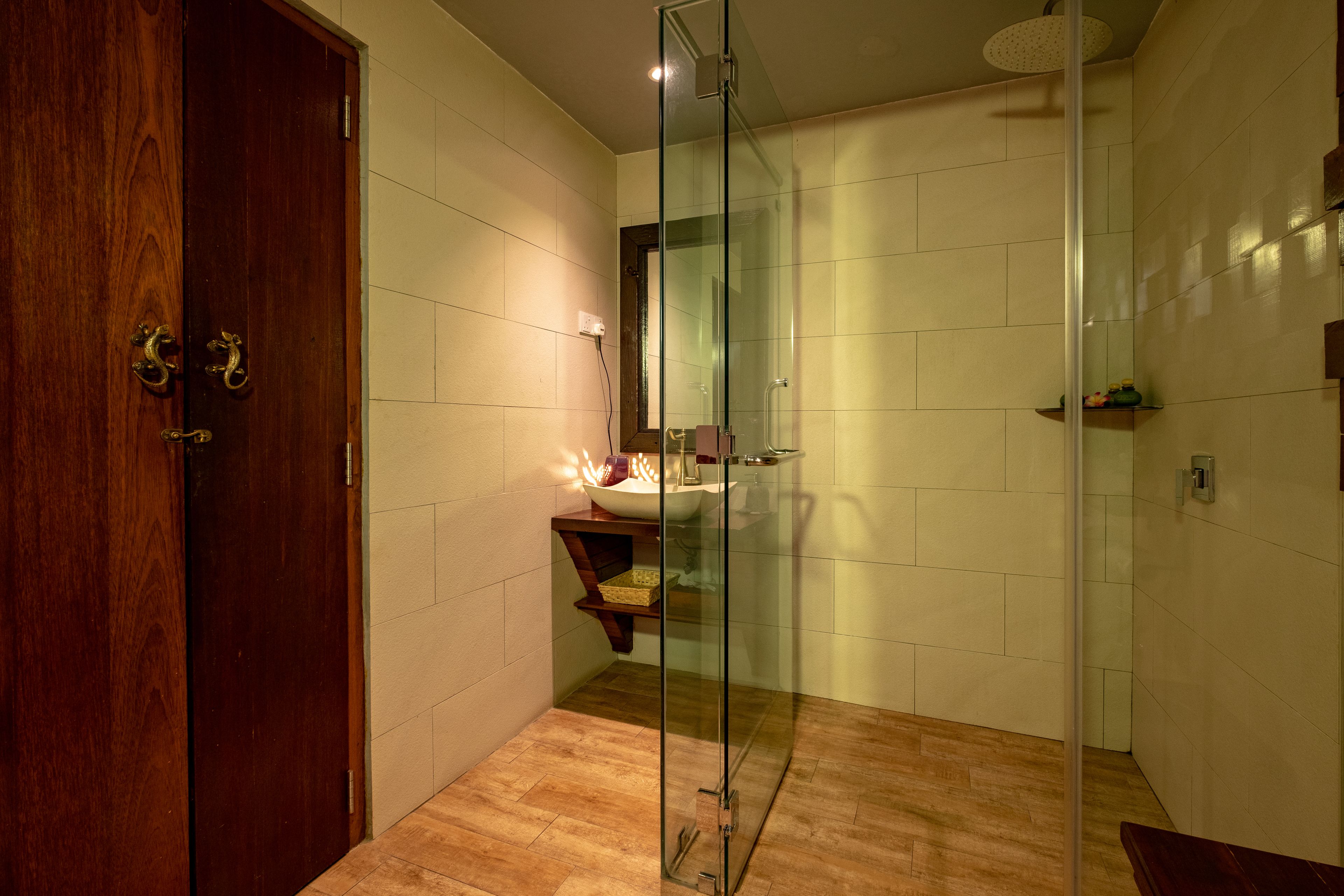 A modern bathroom with a glass shower enclosure, wooden flooring, and a wooden door.