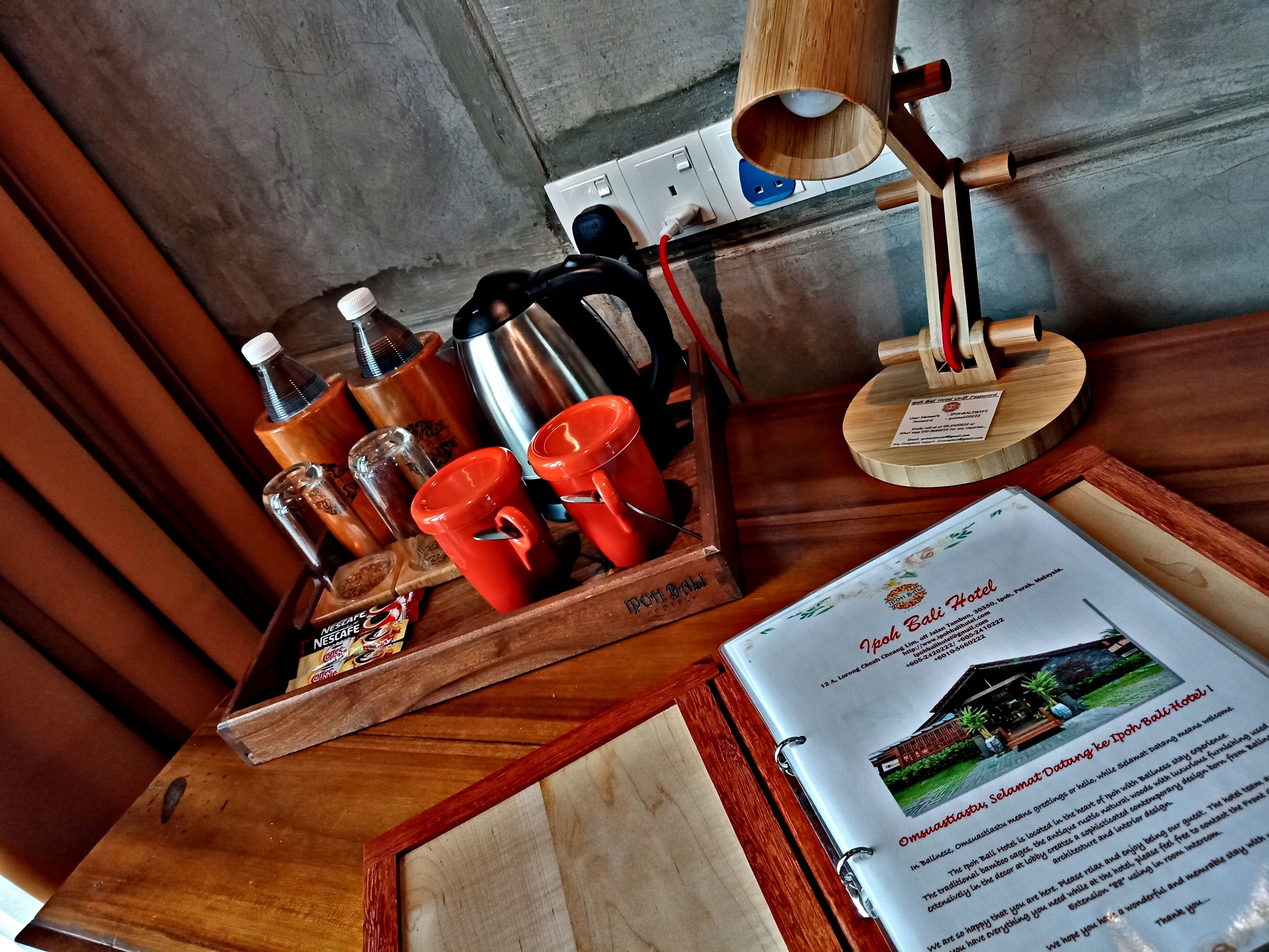 A wooden tray with red cups, a coffee pot, and a bottle on a table.