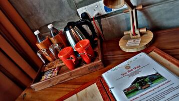 A wooden tray with red cups, a coffee pot, and a bottle on a table.