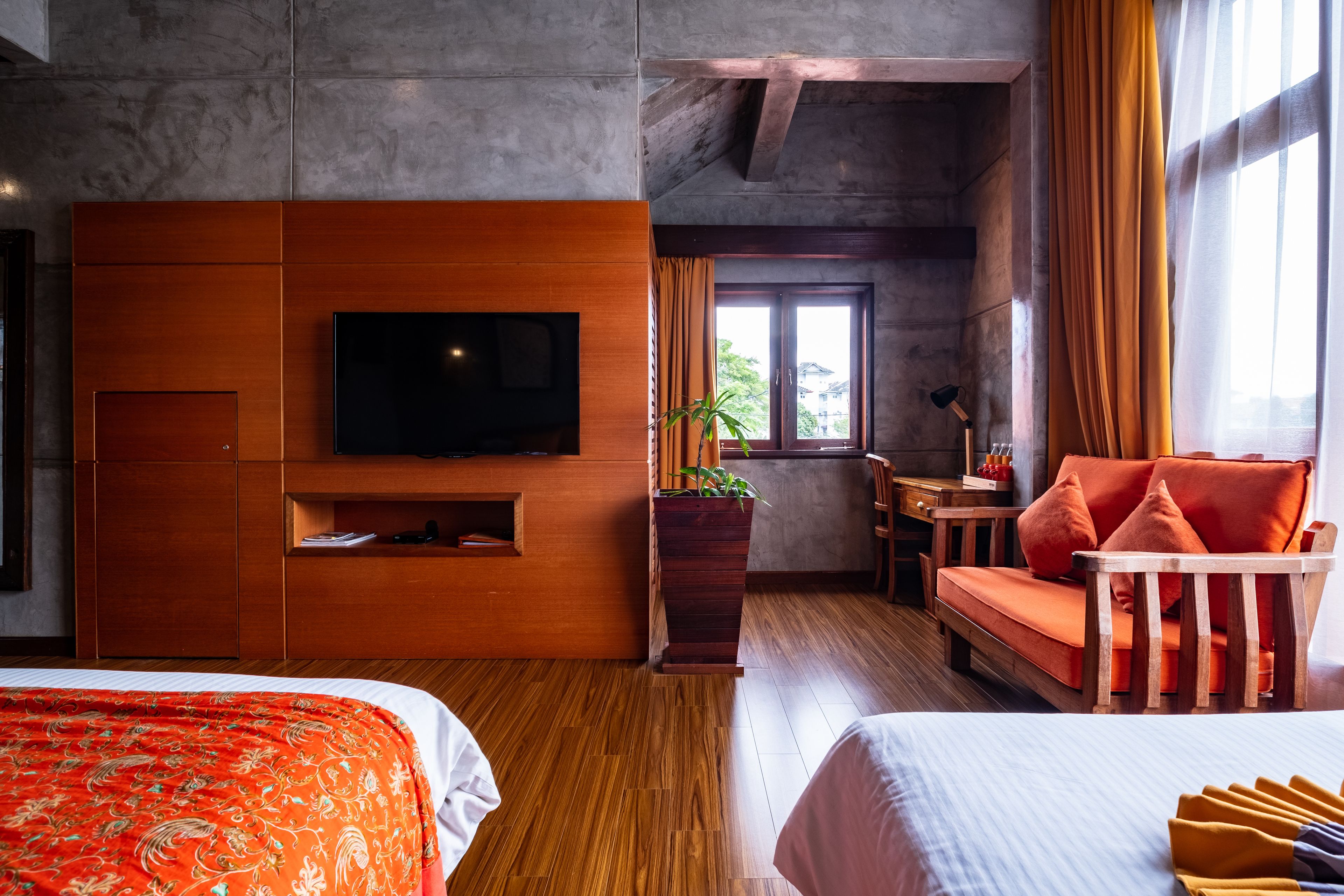 Una habitación de hotel moderna con una cama grande, una cama más pequeña, un televisor, un mueble de madera, una planta, un sofá y una ventana con cortinas.