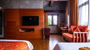 Una habitación de hotel moderna con una cama grande, una cama más pequeña, un televisor, un mueble de madera, una planta, un sofá y una ventana con cortinas.