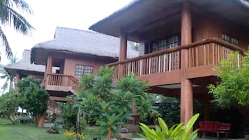 Il s’agit d’un bâtiment traditionnel en bois, doté d’un toit de chaume, d’un balcon et d’un jardin où poussent différentes plantes, ainsi que d’un banc rouge.