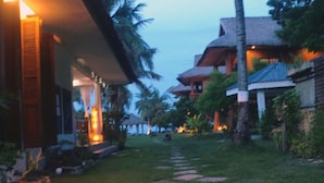 A pathway leading to a building with a thatched roof, surrounded by greenery and palm trees. - Hoyohoy Villas (Santa Fe)