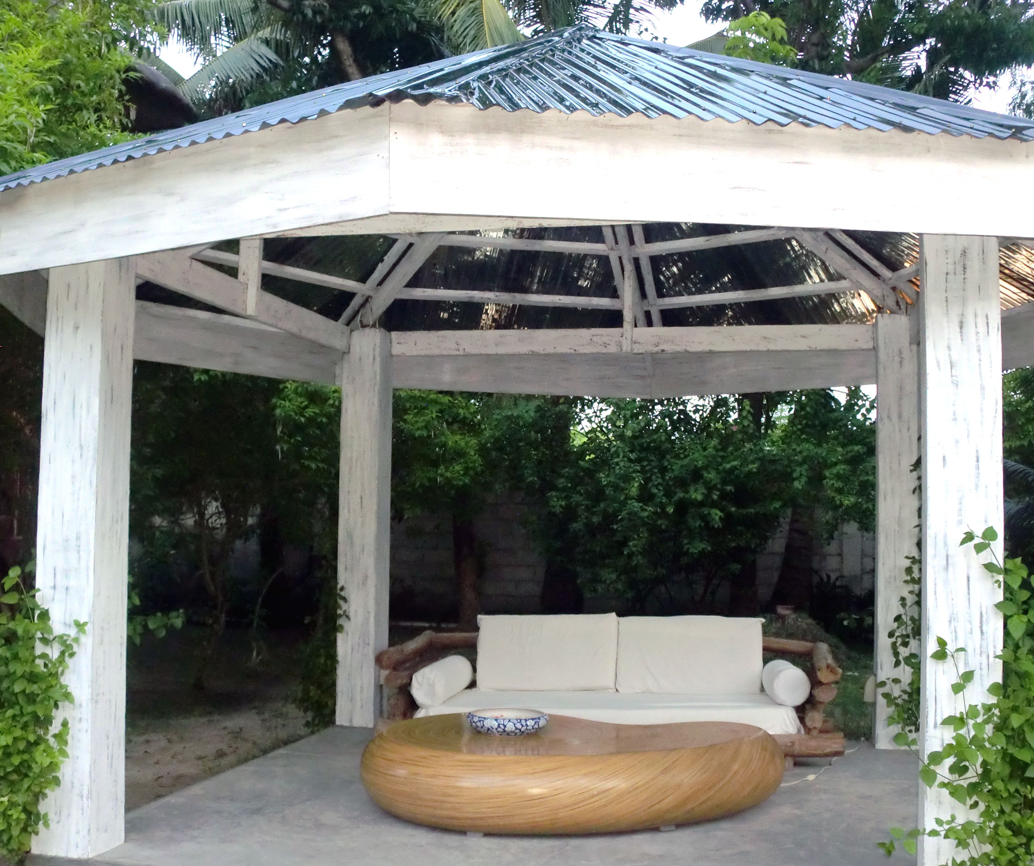 A covered outdoor seating area with a wooden bench and a round wooden table.
