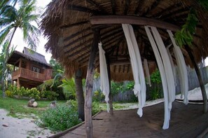 A thatched-roof structure with a wooden deck and hanging white drapes. - Hoyohoy Villas (Santa Fe)