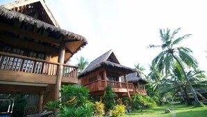 A wooden building with thatched roofs, surrounded by lush greenery and palm trees. - Hoyohoy Villas (Santa Fe)
