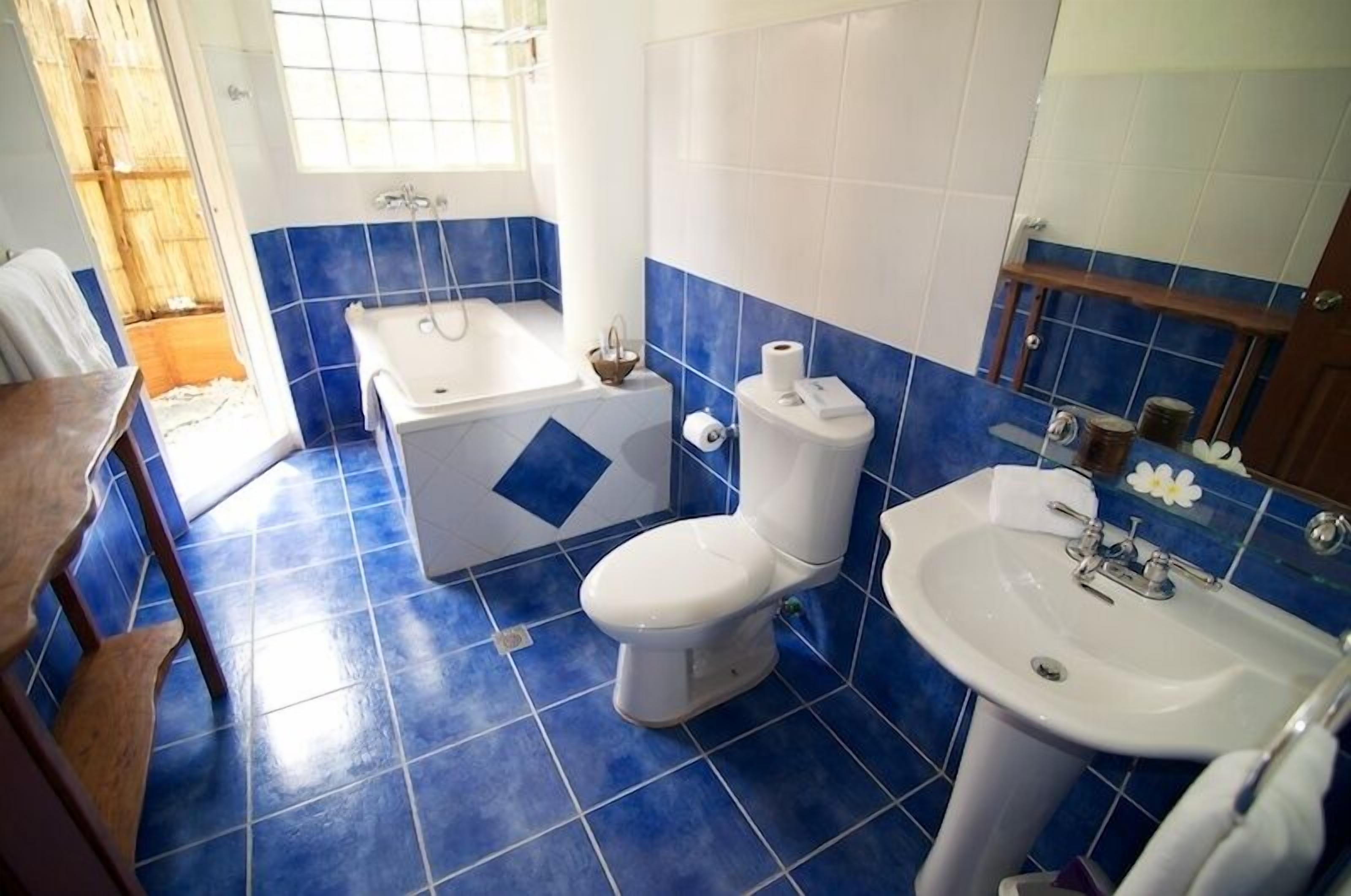 A bathroom with blue tiles, a white toilet, a bathtub, and a sink.