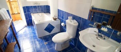 Un baño con azulejos azules, inodoro blanco, bañera y lavamanos.