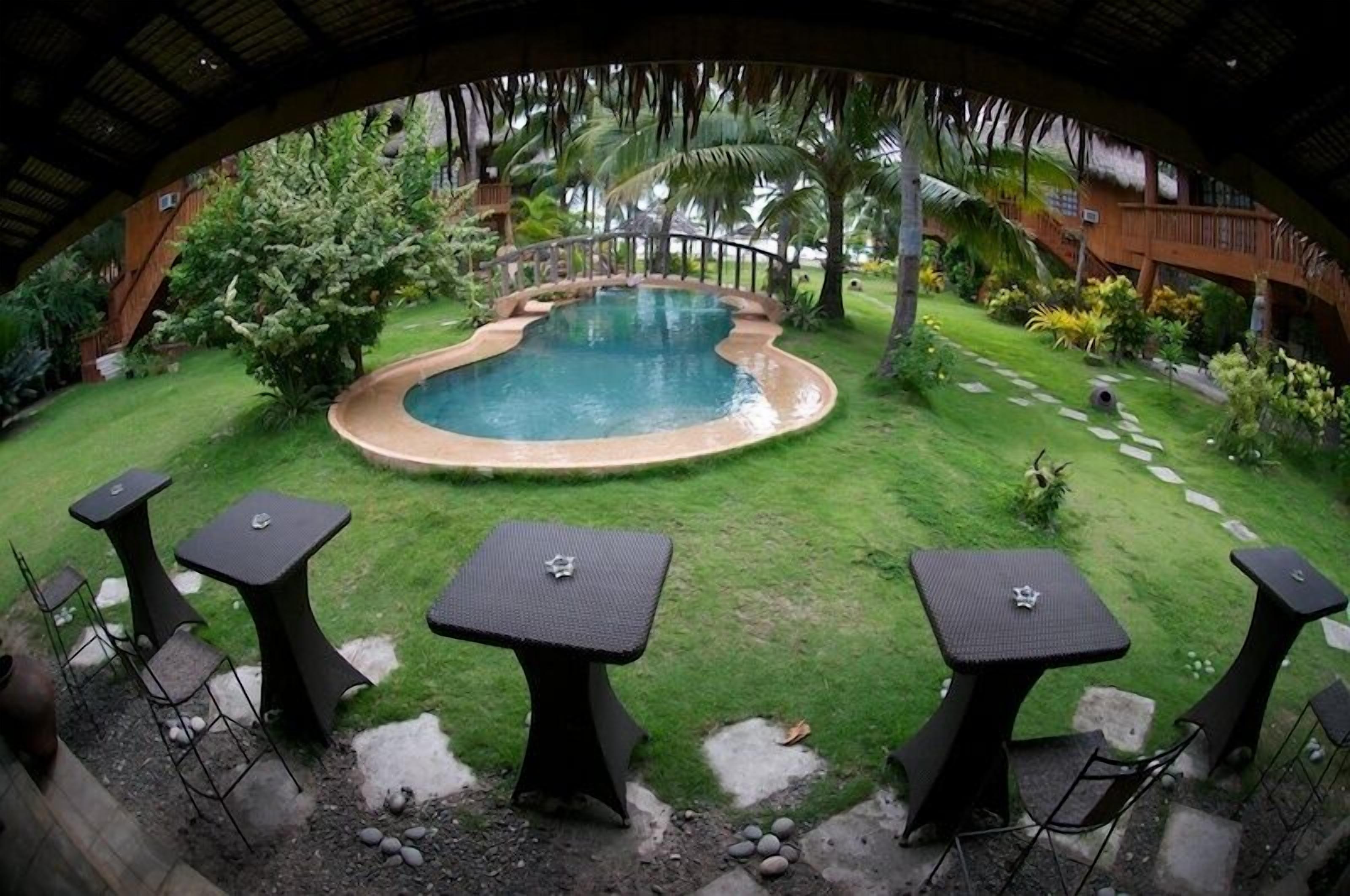 A pool surrounded by a well-maintained lawn, with three tables and chairs arranged for outdoor dining.