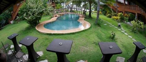 A pool surrounded by a well-maintained lawn, with three tables and chairs arranged for outdoor dining.