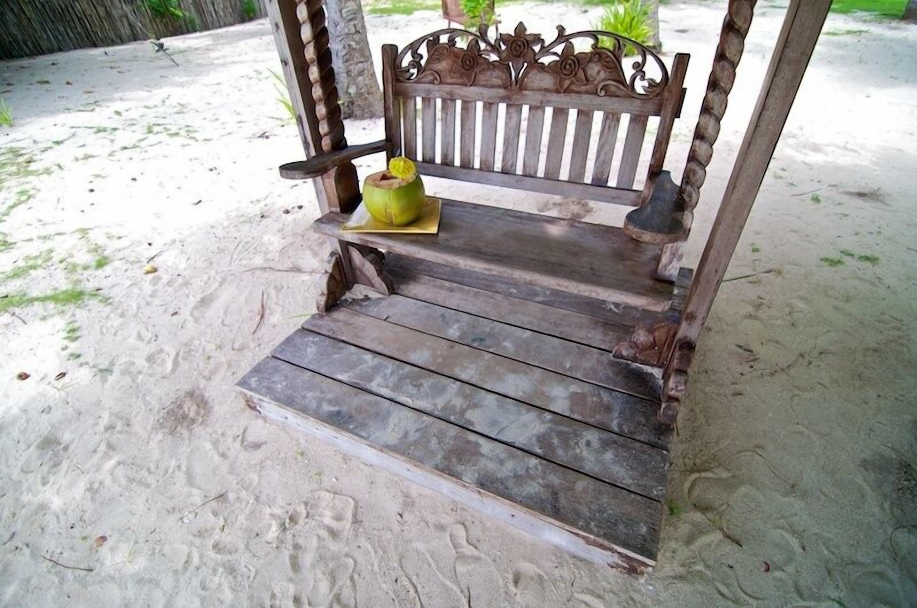 A wooden bench with a carved backrest and a coconut placed on a yellow mat.