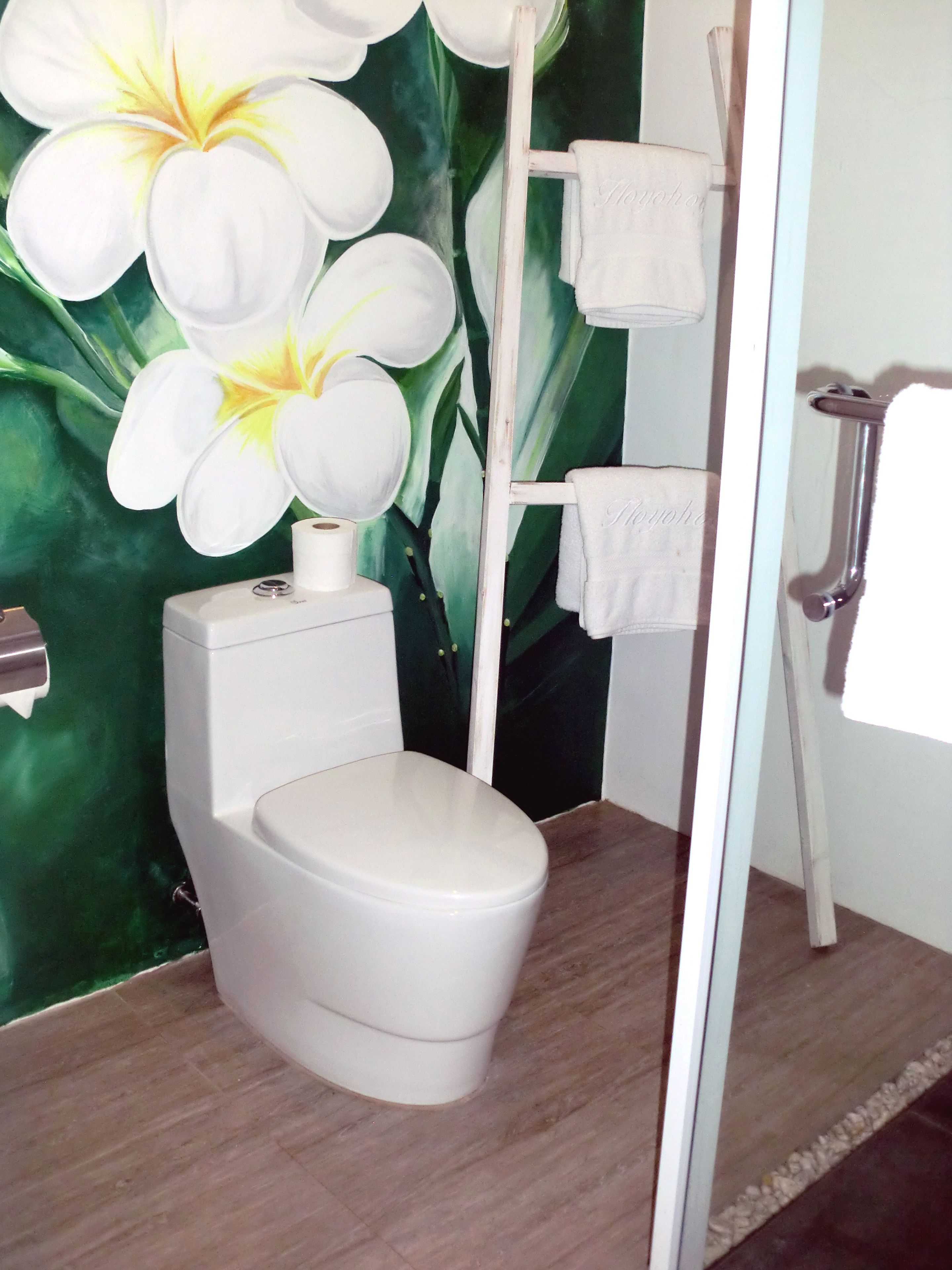 Un baño con inodoro, toallero y un diseño floral verde en la pared.