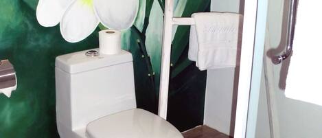 Un baño con inodoro, toallero y un diseño floral verde en la pared.