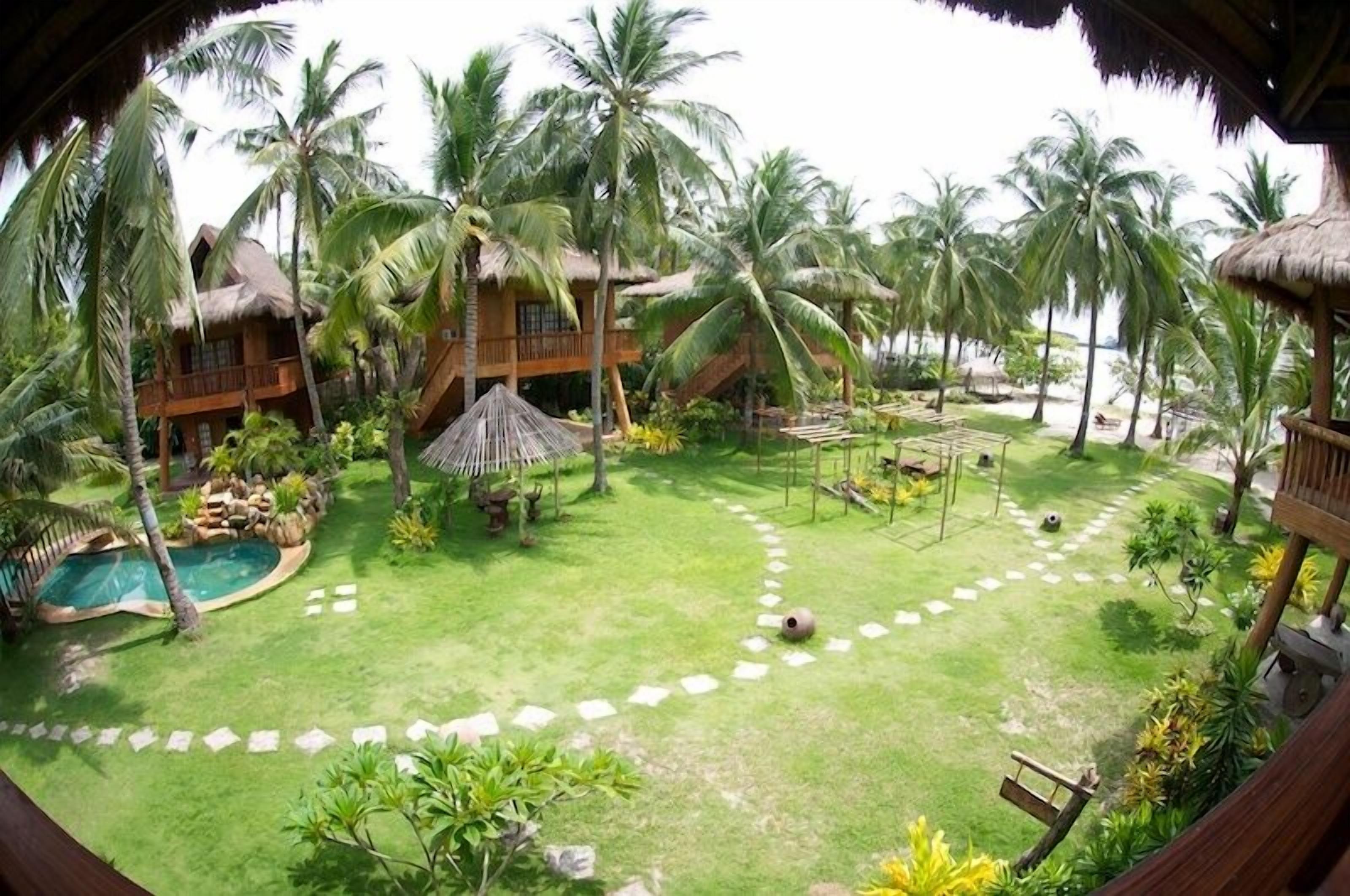 Un resort tropical con piscina, palmeras y una estructura de techo de paja.