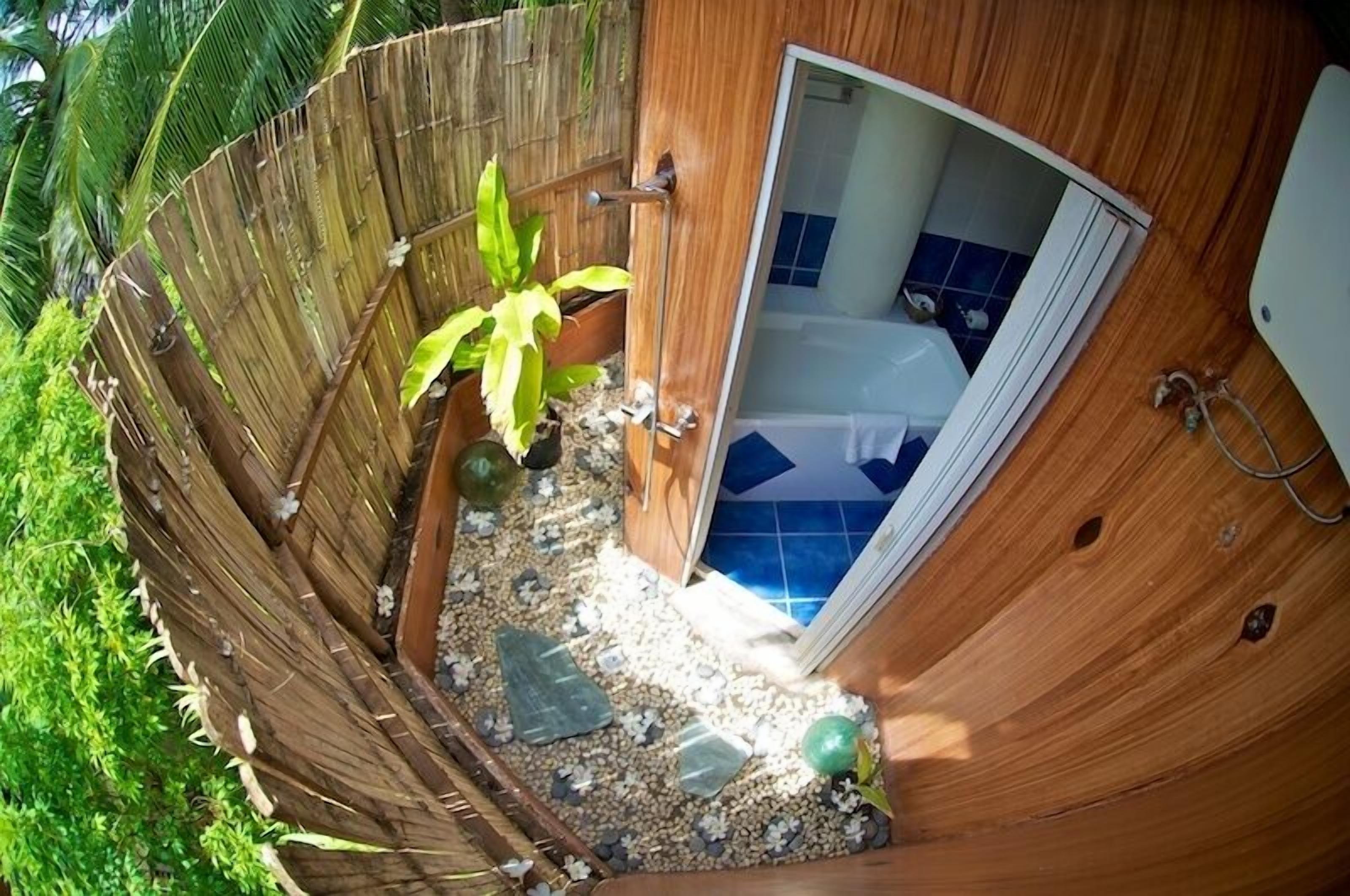 Ein Badezimmer mit einer Badewanne, einer Holztür und einem kleinen Gartenbereich mit Kies und einer Pflanze.