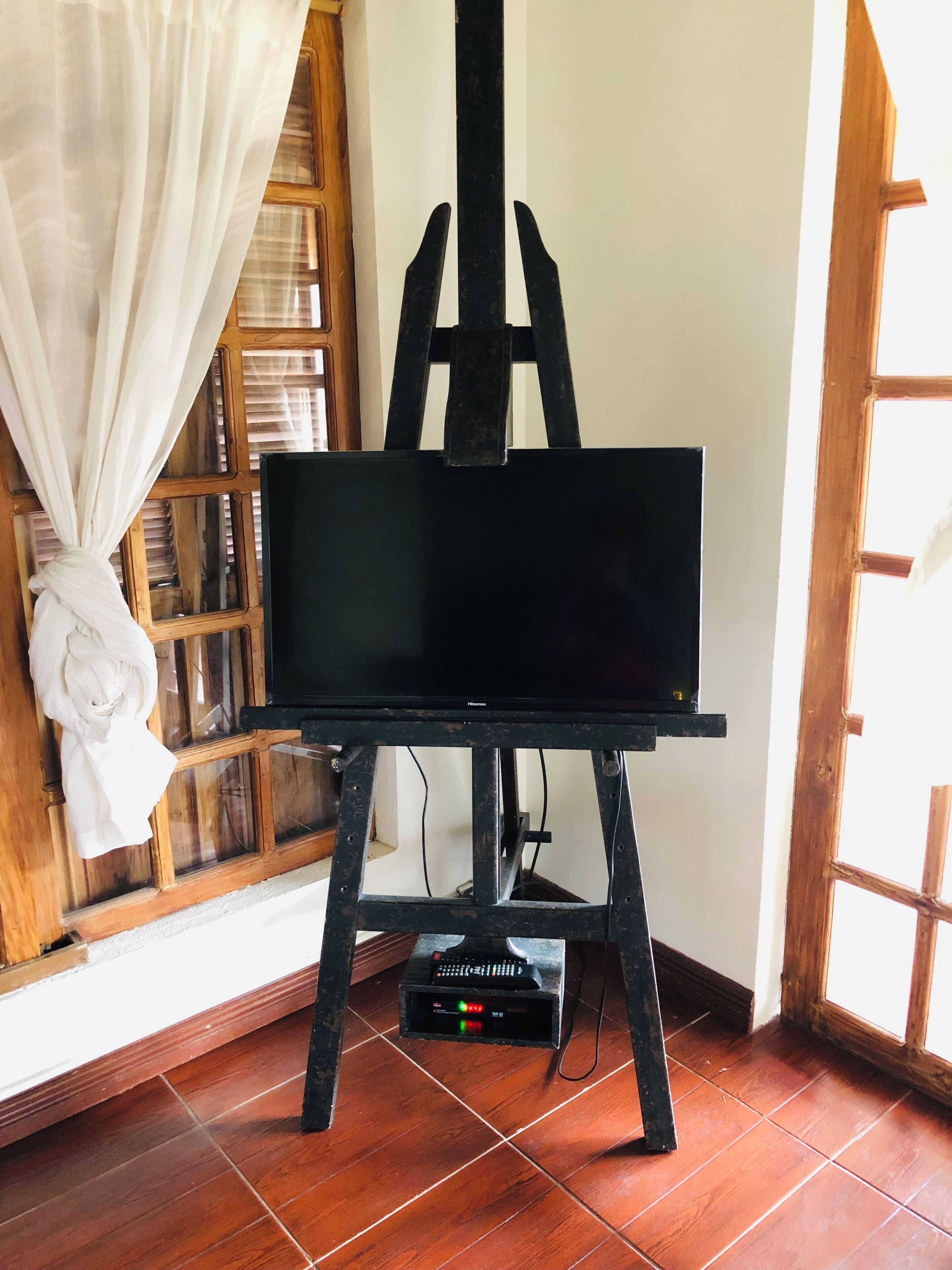 Un televisor negro sobre un soporte de madera en una habitación con suelo de madera y una ventana con cortina.