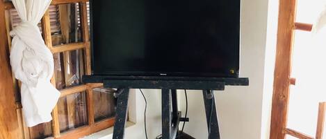 Un televisor negro sobre un soporte de madera en una habitación con suelo de madera y una ventana con cortina.