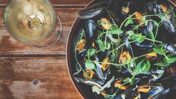 A bowl of mussels with greens on a wooden table.