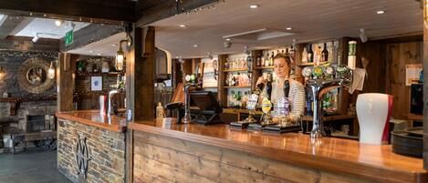 A bar area with wooden counter, shelves of bottles, and a person serving.