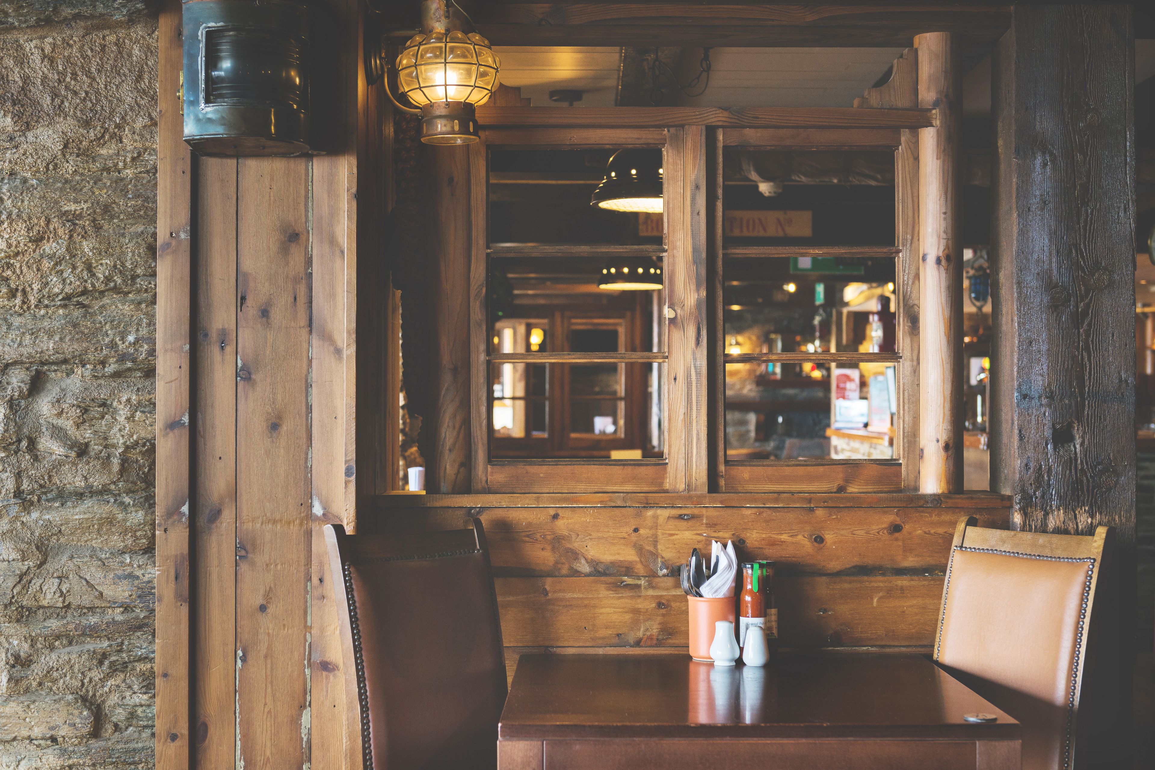 A wooden booth with a table and chairs, a window with a view of the interior, and a hanging light fixture.