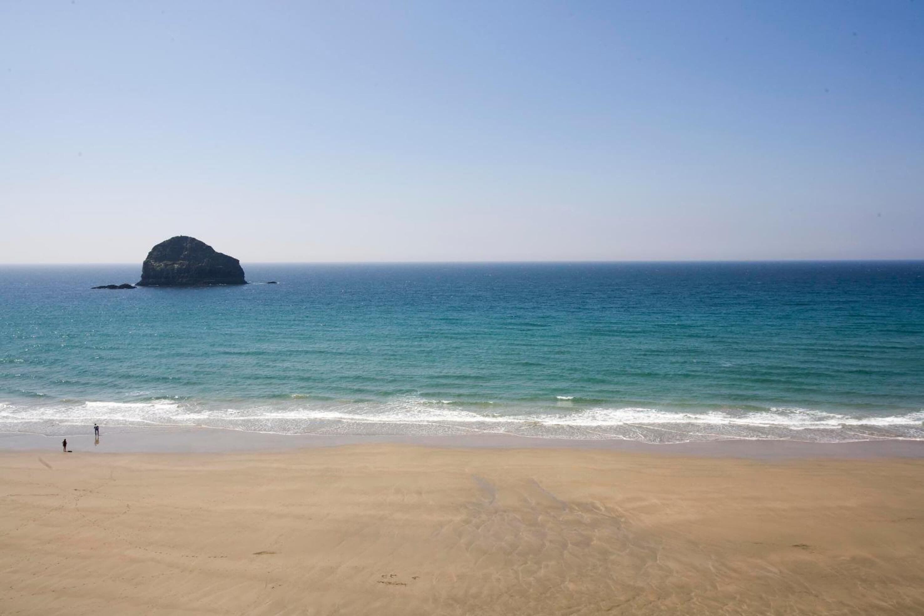 A beach with a large rock formation in the water and a sandy shore.