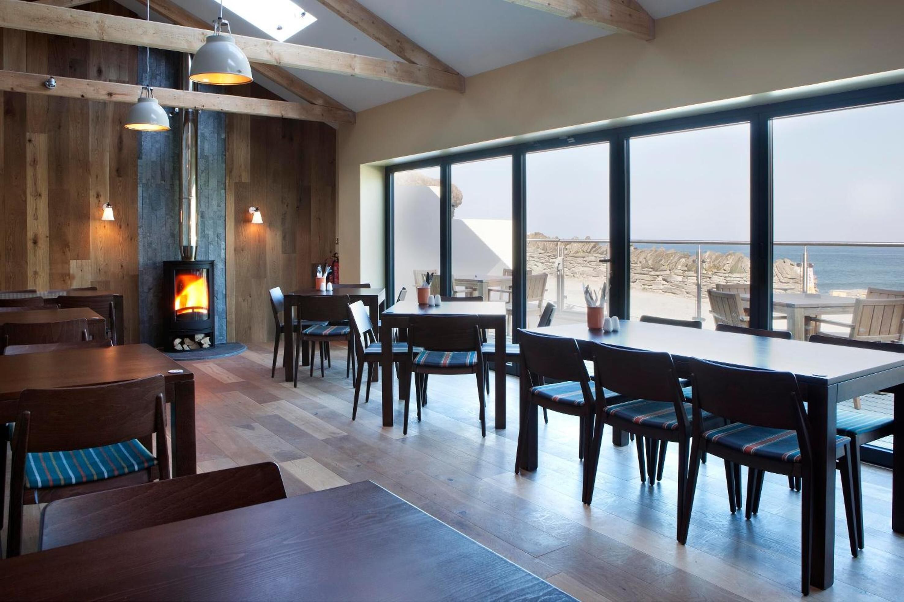 A cozy restaurant with wooden walls, large windows, and a fireplace.