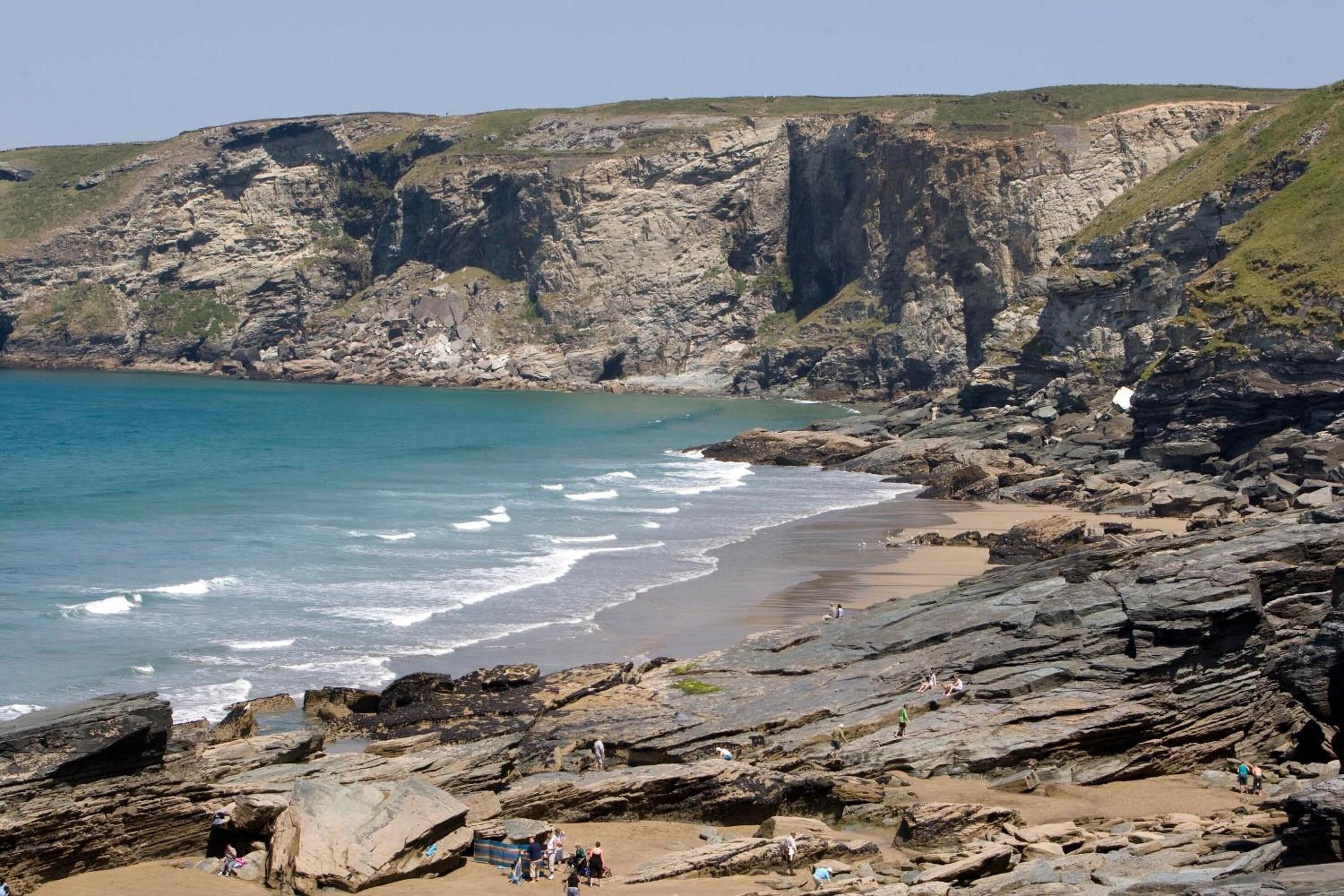 A coastal landscape with rocky cliffs, a sandy beach, and the ocean.